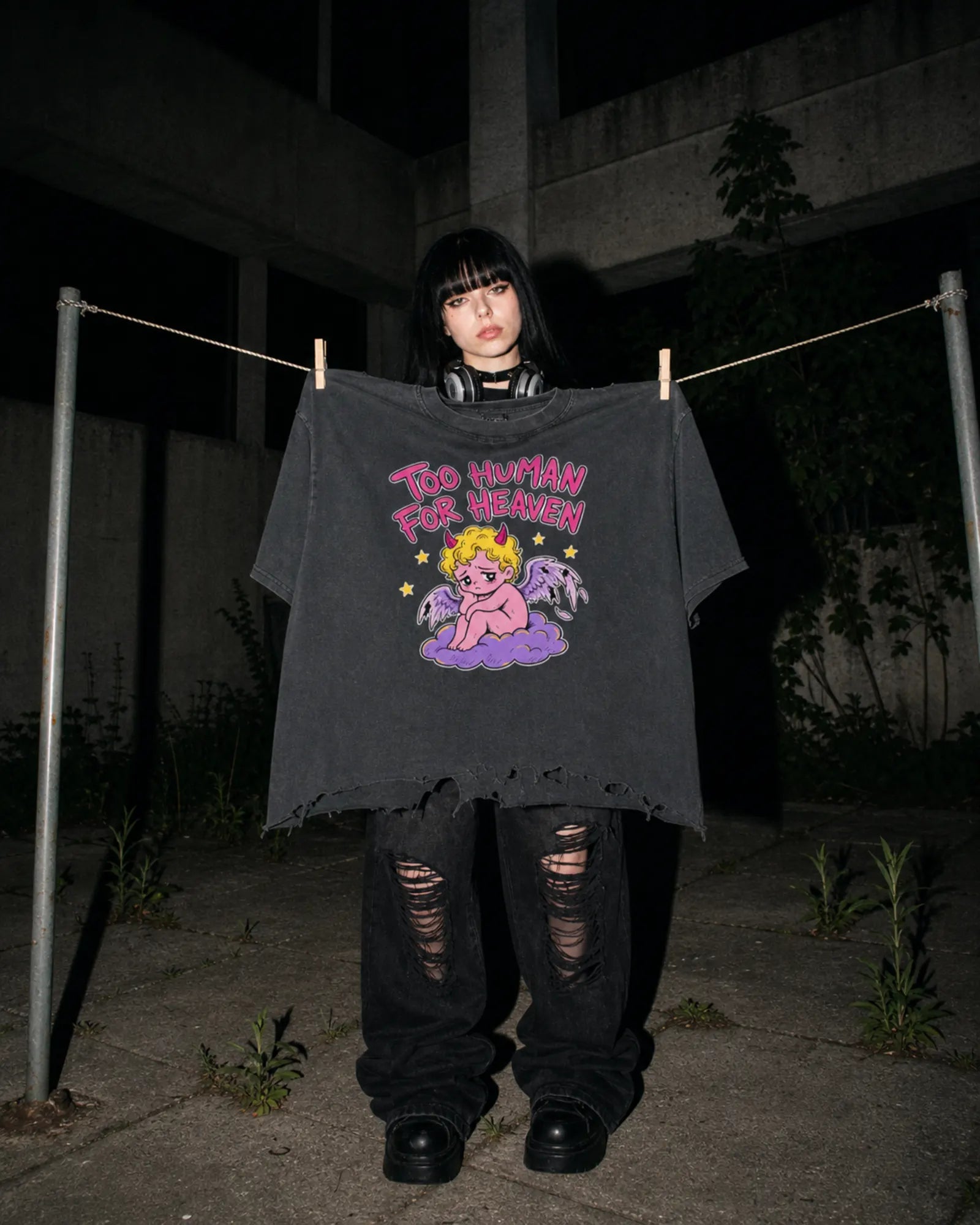 Model at night holding the Too Human For Heaven tee pegged to a clothesline